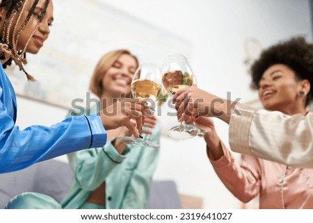 Low angle view of blurred and cheerful multiethnic girlfriends in colorful pajama toasting with wine during girls night at home, bonding time in comfortable sleepwear, slumber party Royalty-Free Stock Photo #2319641027