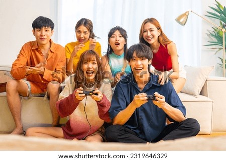Group of Young Asian man and woman playing video games together in living room at home. Happy people friends enjoy and fun indoor activity lifestyle spending time together on holiday vacation. Royalty-Free Stock Photo #2319646329