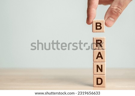 Hand stacking wood cube block with BRAND word on wooden table. Business startup and entrepreneur concept. Marketing Royalty-Free Stock Photo #2319656633