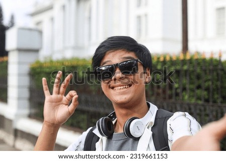 POV of attractive young tourist student man wearing sunglasses smiling funny face and showing ok sign