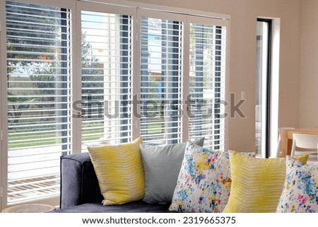 
Open white shutters in living room, with blue couch and yellow scatter cushions Royalty-Free Stock Photo #2319665375