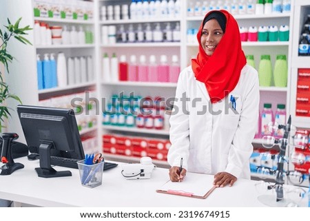 Young beautiful woman pharmacist smiling confident writing on document at pharmacy