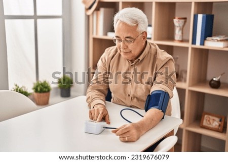 Senior man using tensiometer sitting on table at home