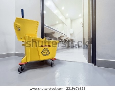 Yellow mop bucket, floor cleaning bucket in front of toilets, concept for cleaning service