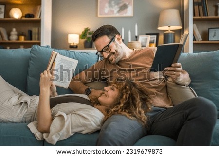 Adult couple man and woman Caucasian husband and wife in a relationship real book hold books on the sofa bed at home in the apartment reading leisure bonding family concept real people copy space Royalty-Free Stock Photo #2319679873
