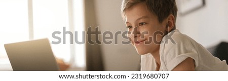 Young boy lies on the bed and looks into an open laptop. Home education concept