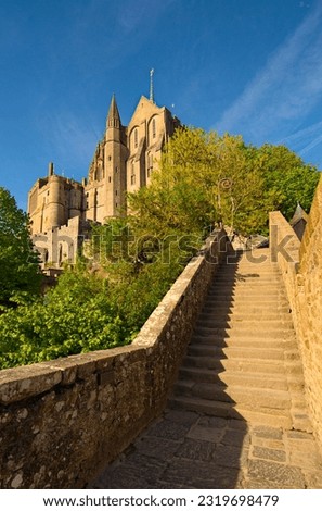 Ancient narrow cobblestone stairs to the medieval Mont Saint-Michel Abbey. Scenic landscape photo at sunny spring day. Normandy, France. Travel and tourism concept. UNESCO World Heritage Site.