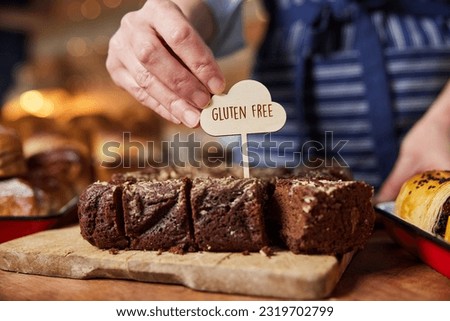 Sales Assistant In Bakery Putting Gluten Free Label Into Freshly Baked Brownies Royalty-Free Stock Photo #2319702799