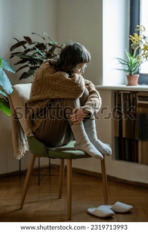 Depression in teens. Lonely depressed teen girl hugging knees sitting alone on chair at home, sad adolescent female feeling unattractive and unhappy. Teenage loneliness and social isolation Royalty-Free Stock Photo #2319713993