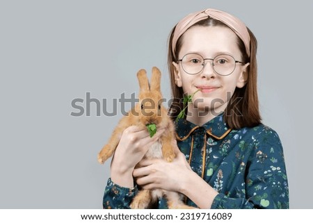 A beautiful little girl in glasses poses with a rabbit that eats parsley.
