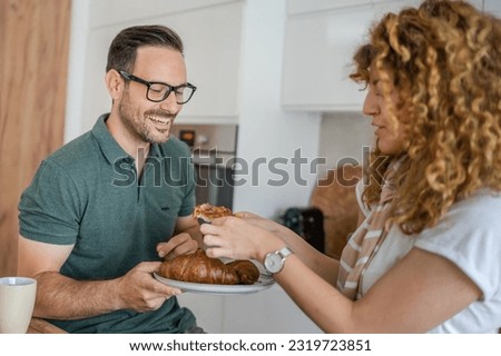 Caucasian couple man and woman having breakfast in the kitchen eat croissant and coffee daily morning routine domestic family life real people copy space