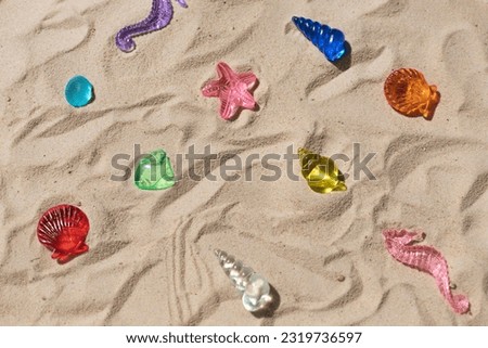 Marine transparent colorful figurines or kid's toys on the beach sand. Summer sea vacation concept background