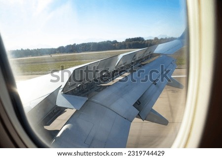 View from the porthole of an airplane wing taking off over the runway at high speed during sunset. The ground passes under the wing. Royalty-Free Stock Photo #2319744429