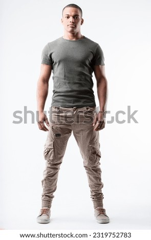 Fit young black man, V-shaped chest, lean waist in a relaxed yet strong pose. Very short hair, military-inspired outfit, low sneakers, slight smile. Full frontal portrait, isolated from background