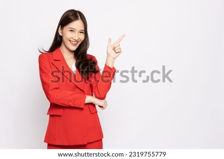 Young beautiful Asian businesswoman in red suit smiling and pointing to empty copy space isolated on white background