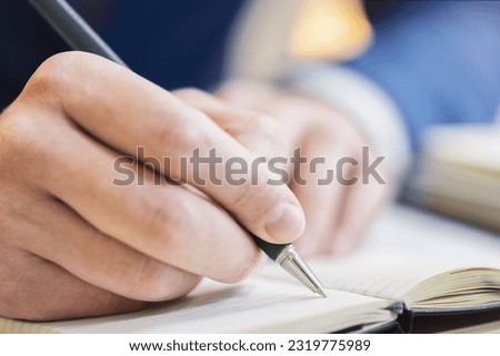 Close-up capture of a man's hand as he writes in a notepad, with an out-of-focus background Royalty-Free Stock Photo #2319775989