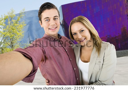 Young couple taking a selfi in front of one of the highlights of a city trip, holding eachother