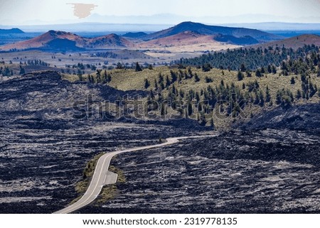 Road that runs between lava rocks and grasslands with pine trees. Craters of the Moon National Monument and Preserve is a United States National Monument and National Preserve on the Snake River Plain