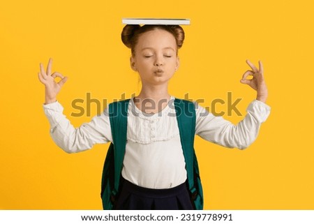 Keep Calm. Cute Little Schoolgirl Meditating With Book On Head And Closed Eyes, Adorable Female Child Coping With Learning Stress, Standing Isolated On Yellow Background, Copy Space