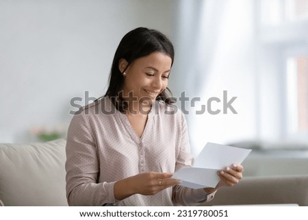 Happy young mixed race woman holding and reading paper letter, receiving invitation or good news about approved loan, mortgage, tax, insurance, getting notice about acceptance of statement Royalty-Free Stock Photo #2319780051