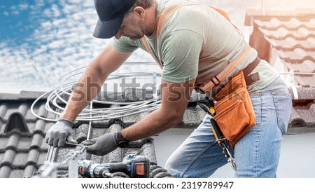 Work on the roof. An electrician`s hands turning screw using a spanner during installing a lightning rod conductor on a tiles roof.