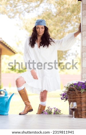 A beautiful woman is wearing a white dress and a blue headband. Resting on a ranch