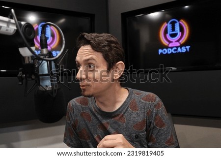 young, white man doing podcast, irreverent, funny, intriguing, in bright, colorful podcast room, with microphones and television