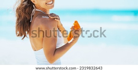Smiling young woman on beach applying sun block creme Royalty-Free Stock Photo #2319832643