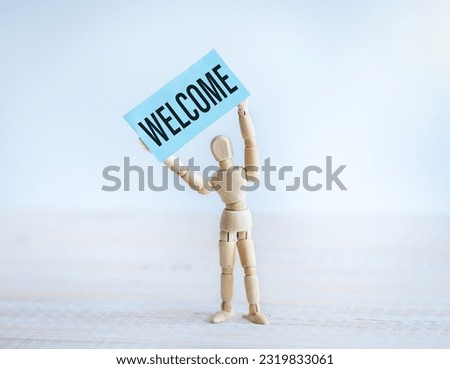 Welcome Text on Paper in the Hands of a Wooden Man.
