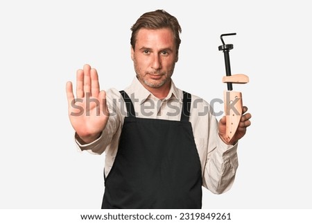 A middle-aged shoe maker standing with outstretched hand showing stop sign, preventing you.