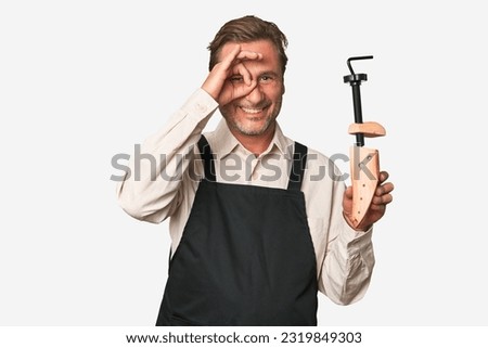 A middle-aged shoe maker excited keeping ok gesture on eye.