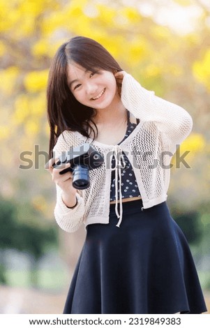 Portrait cute smiles Asian of attractive young teenage girl a holding the camera in blooming Yellow Golden Tabebuia Chrysotricha flowers with the park in spring day at Evening background in Thailand.