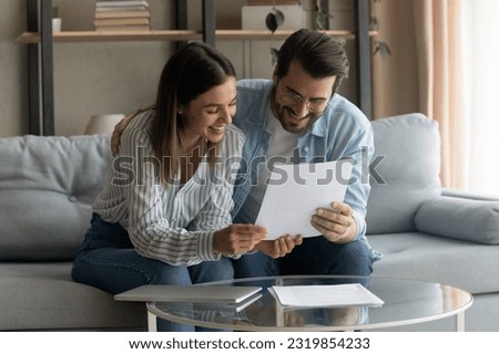 Smiling husband and wife sit on sofa reading received formal letter from bank about debt repayment, loan mortgage offer, reviewing together agreement, got invitation notice, health insurance concept Royalty-Free Stock Photo #2319854233