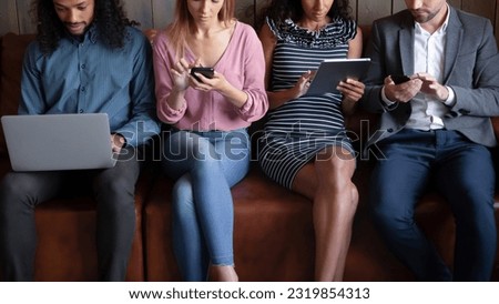 Cropped image addicted to modern technology four young diverse mixed race people sitting on sofa, involved in using different gadgets, spending time online in social networks, remote job concept.
