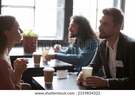 Interested young mixed race people with badges on clothes involved in conversation, attending speed dating in cafeteria. Happy millennial generation multiracial men and women seeking for relations. Royalty-Free Stock Photo #2319854323