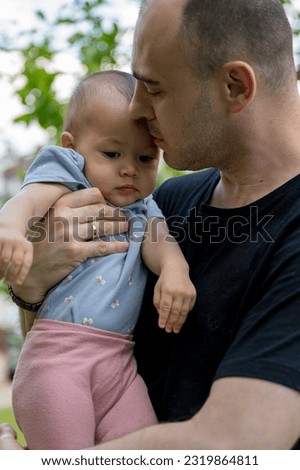 Father and daughter sitting at the garden, kissing and holding the baby