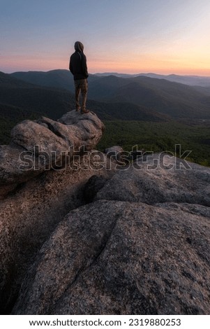 A hiker poses at sunrise atop a boulder on the summit of Old Rag in Shenandoah National Park, Virginia.