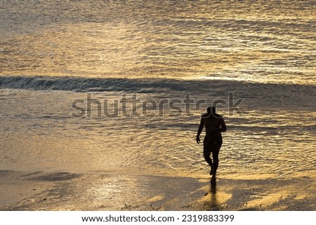 The silhouette of a man emerging from the sea on the beach of Jericoacoara, Ceará, during sunset