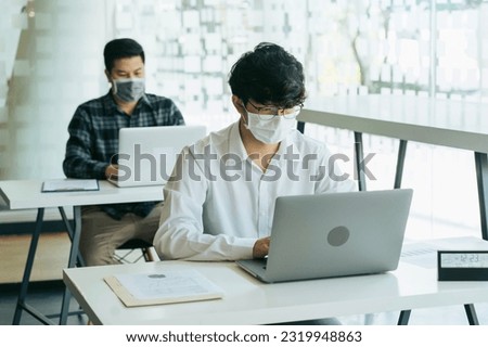 Asian colleague works while wearing a mask in the office during COVID-19.