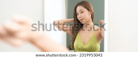 Get dress, elegant asian young woman makeup getting ready wearing green cloth, gorgeous or glamour female check, looking into mirror in bedroom at home, prepare going event night party, celebration. Royalty-Free Stock Photo #2319953043
