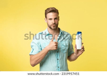 man hold shampoo cosmetics isolated on yellow, thumb up. man hold shampoo cosmetics in studio