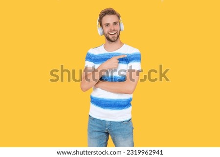 man listen and enjoys live music, point finger. man listens to music on headphones isolated on yellow. man relaxes and listens to music in studio. man uses his wireless headphones to listen to music