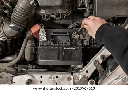 Disconnecting a car starter battery negative terminal after loosening nut with a wrench for taking the dead battery off to replace with new one Royalty-Free Stock Photo #2319967613