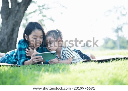 Southeast Asian girls play mobile phones outdoors in the courtyard during the summer on vacation.