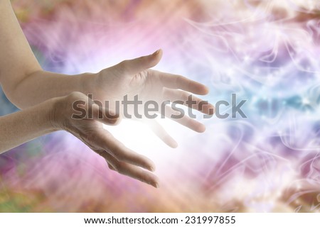 Outstretched female healing hands with white light between and vibrant energy field in background 