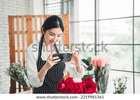 Beautiful florist uses a smartphone to take a picture of beautifully arranged flowers with a lively smile on her face to promote the shop on social media.