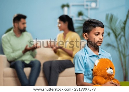 Indian sad kid with doll in front shouting and arguing couple at home - concept of family conflict, childhood trauma and emotional distress. Royalty-Free Stock Photo #2319997579