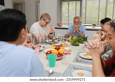 Group of happy diversity multiethnic family with different ages enjoy praying before eating breakfast or dessert in kitchen room at home. Happiness and healthy lifestyle concept.