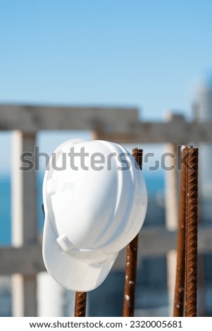 Close-up of a white helmet hanging on a rebar on a construction site on a sunny day. Construction concept, safety techniques. Vertical photo