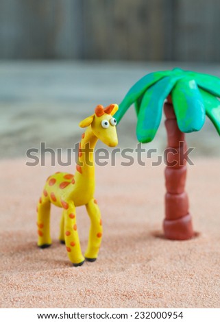 Plasticine world - little homemade yellow giraffe with orange spots and palm on a wooden background, selective focus and place for text